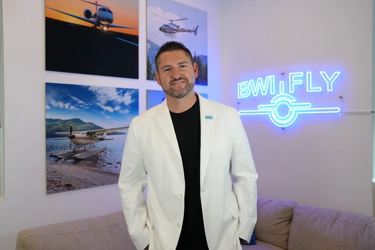 Matt White standing in a white suit beside the BWI sign