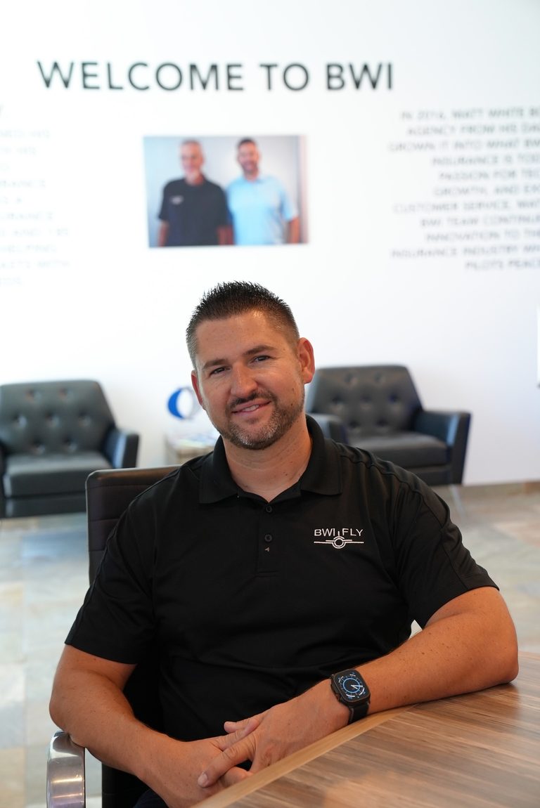 Matt White seated in a black BWI polo at the office, with the Welcome to BWI wall behind him