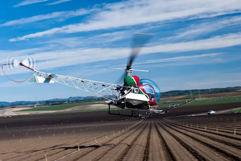 Bell 47 helicopter flying low over farm fields