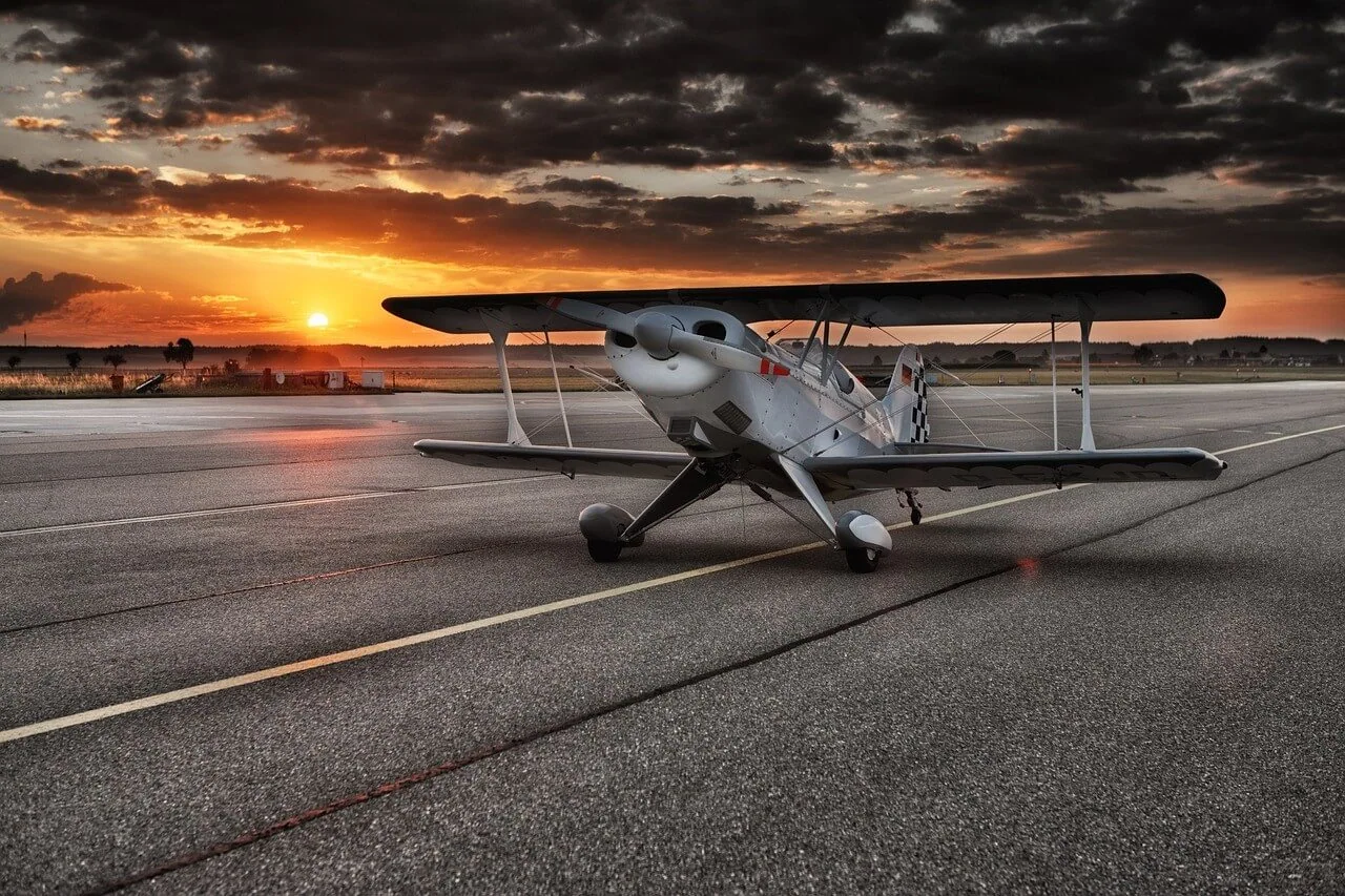 A biplane parked on an airport apron at sunset