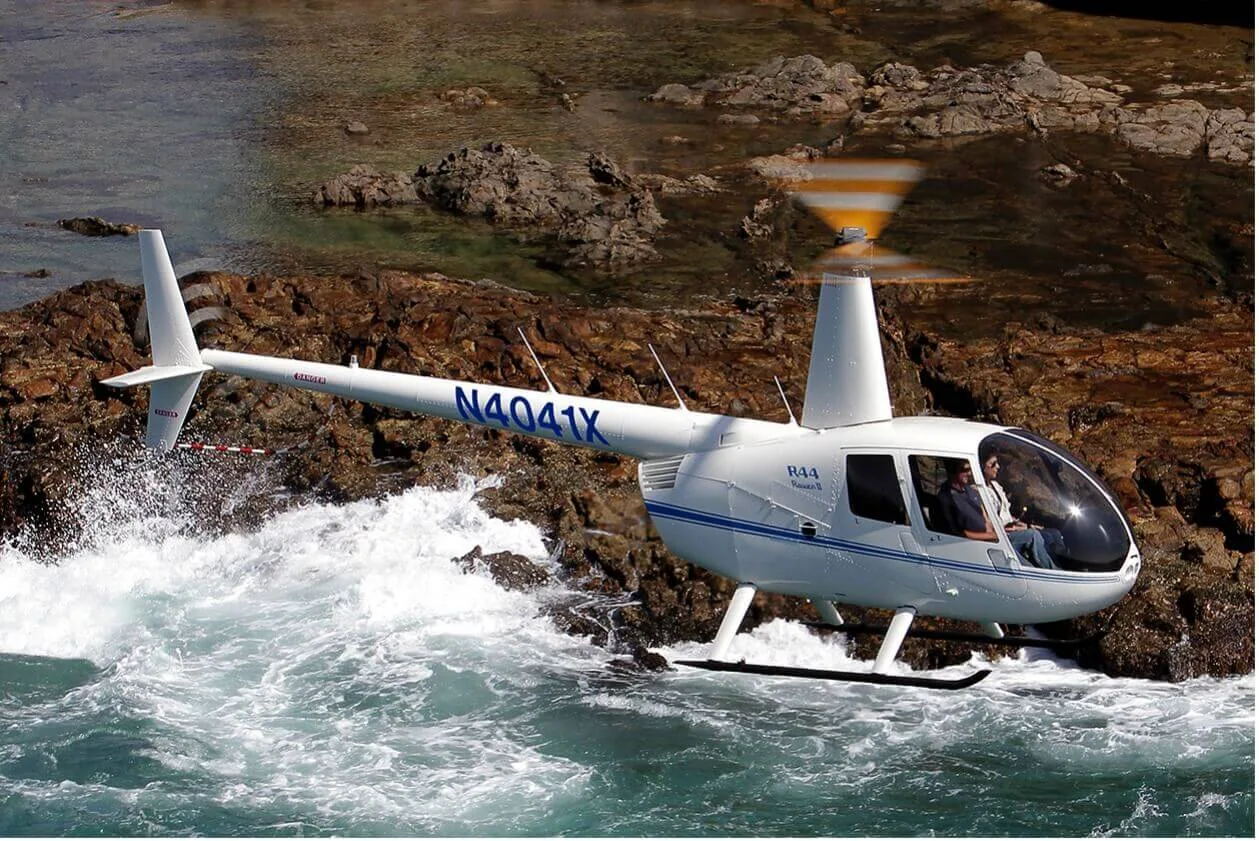 A Robinson R44 helicopter flying above a rocky coastline