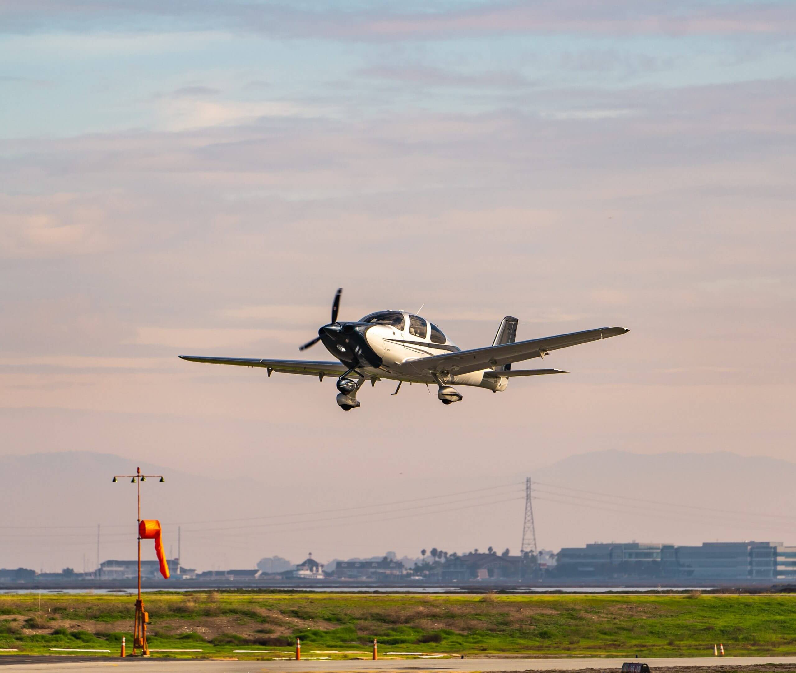 A Cirrus SR20 flying above the runway in warm evening light