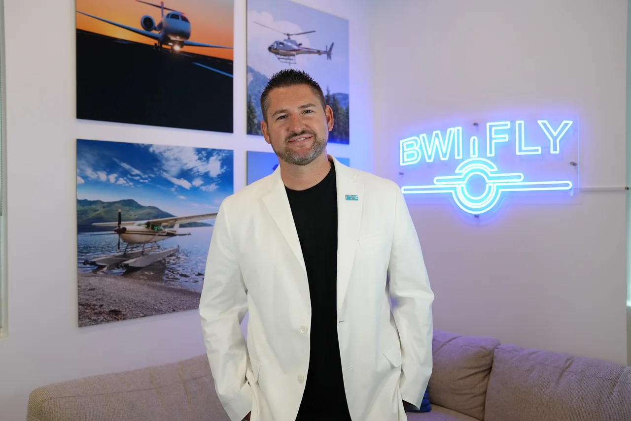 Matt White, Owner and CEO of BWI, in a white suit beside the office couch, aviation photographs and BWI sign
