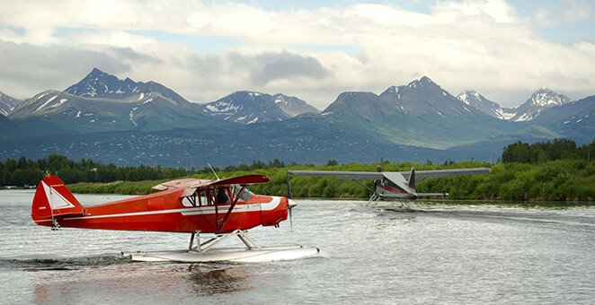 Red and white floatplane on water with mountains behind it