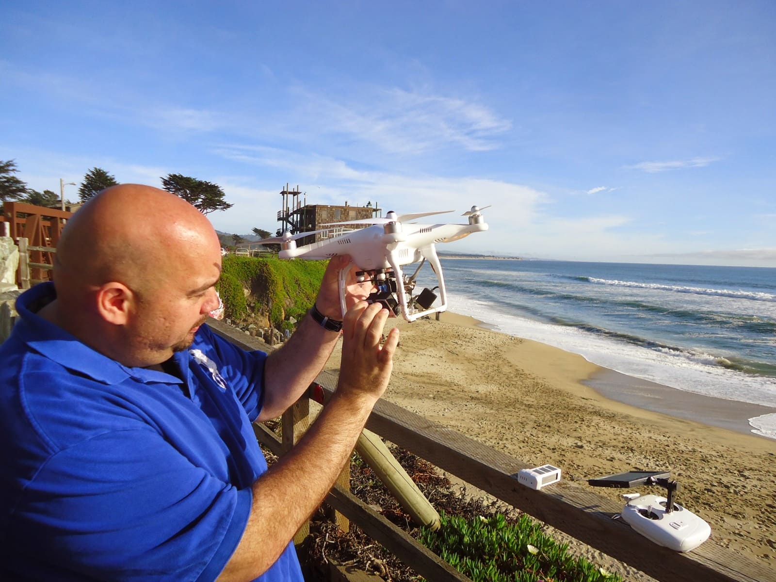 Person holding a white camera quadcopter beside a coastal railing