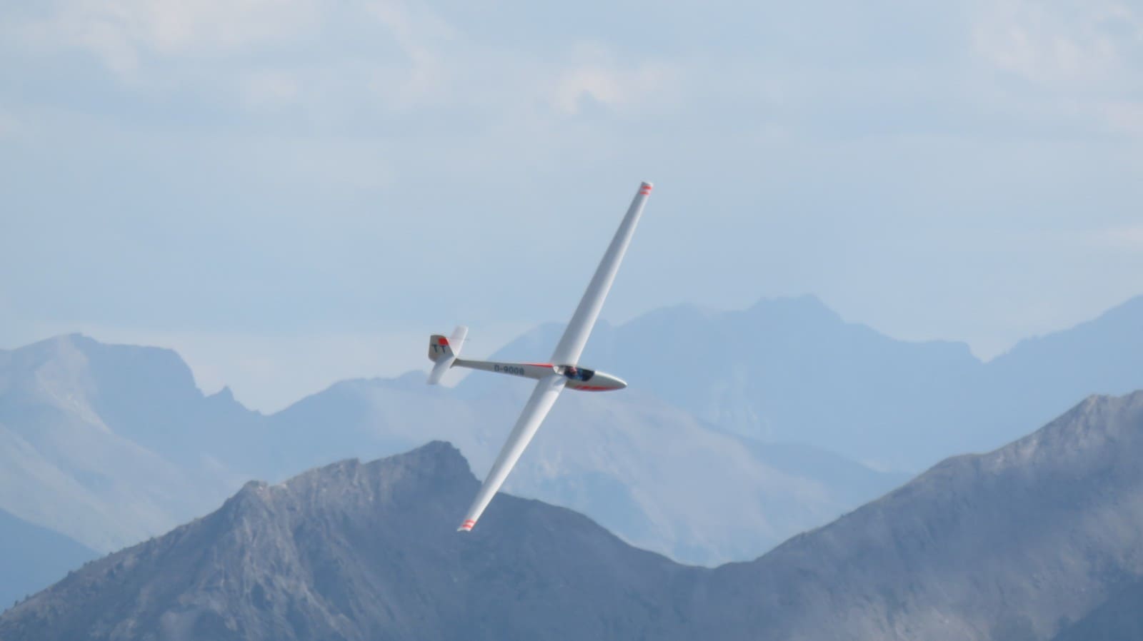 White sailplane banking in front of mountains in the French Alps