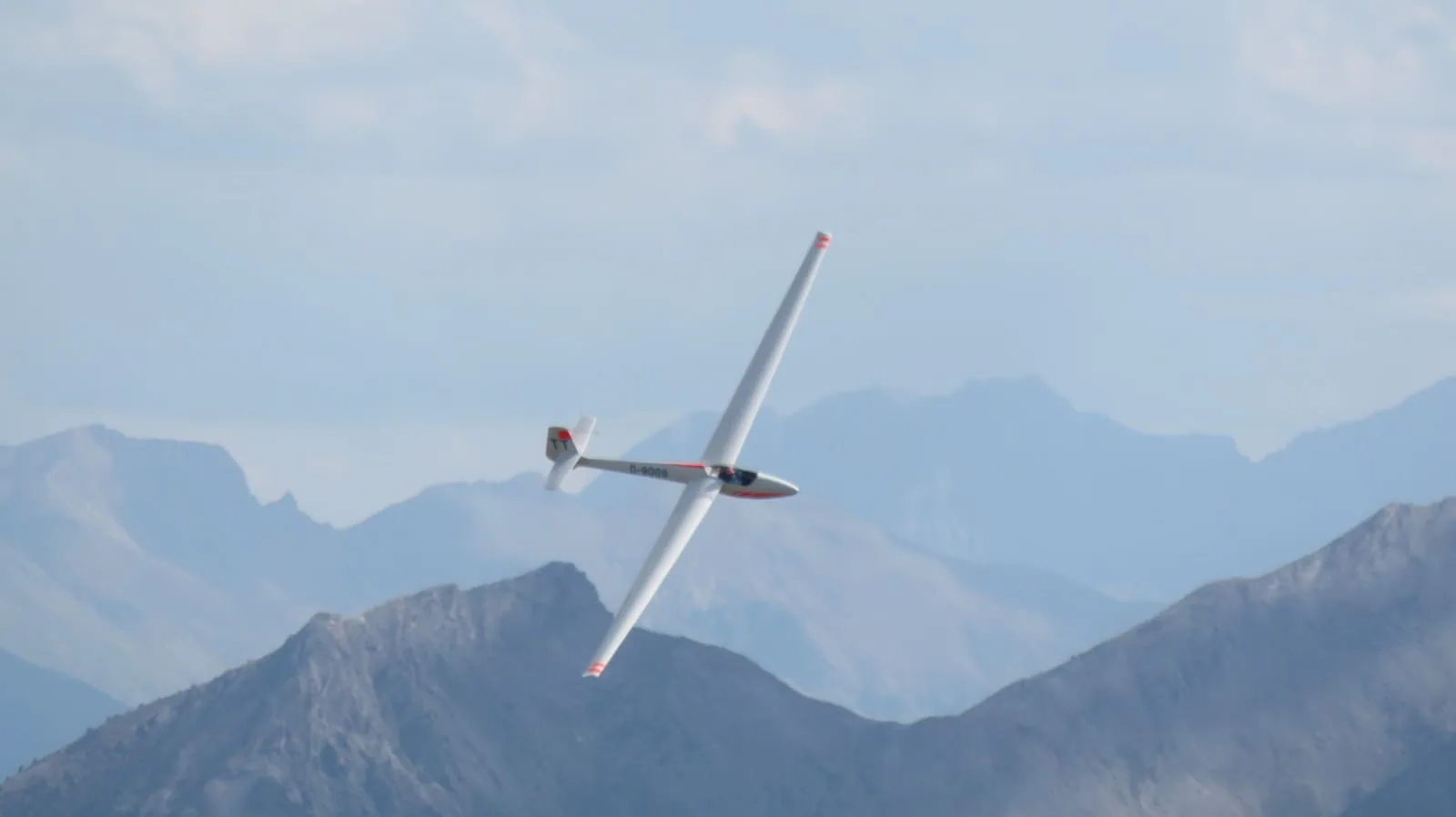 White sailplane flying over mountains in the French Alps