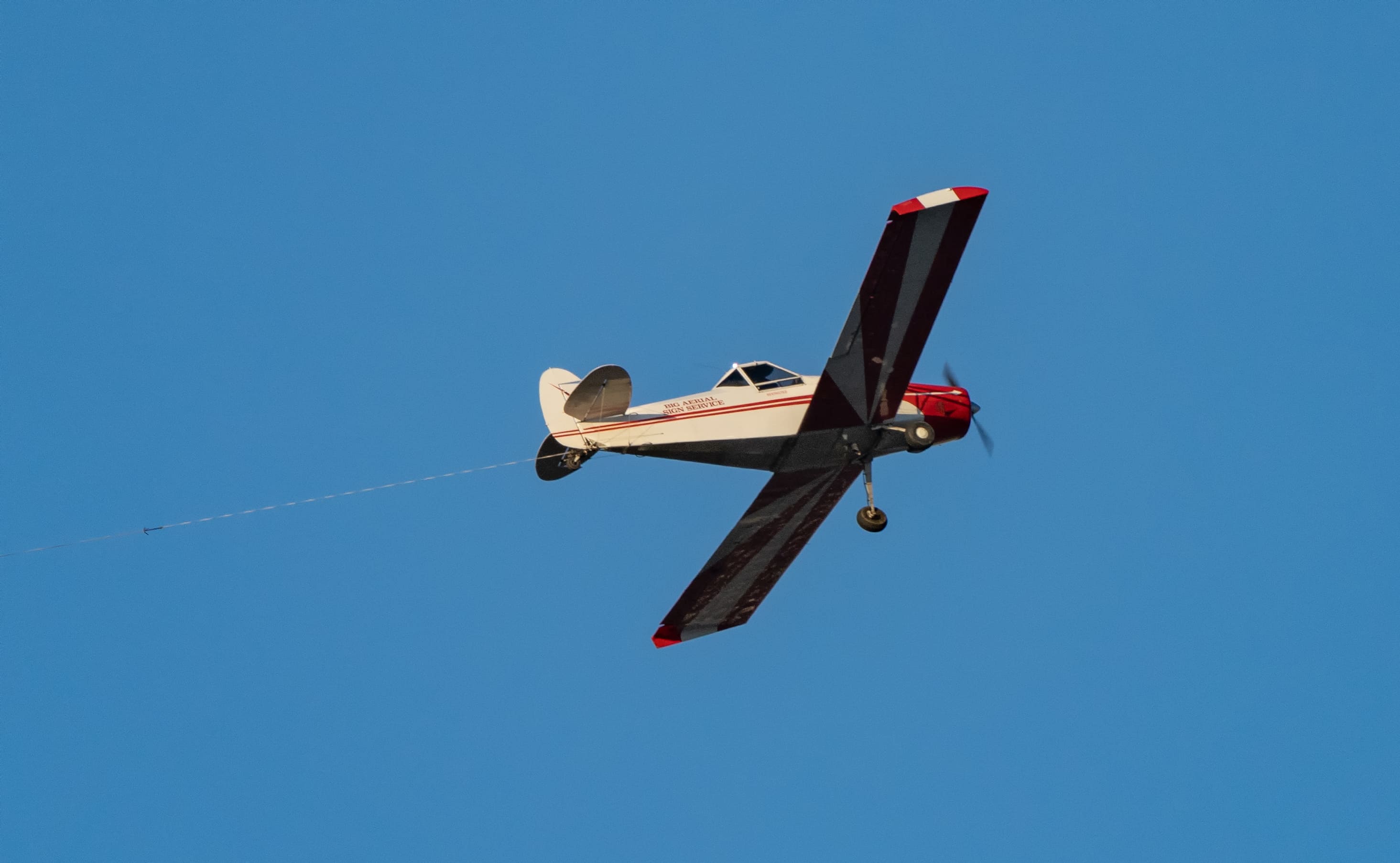 Red and white aerial advertising airplane in flight with a tow line extending behind it