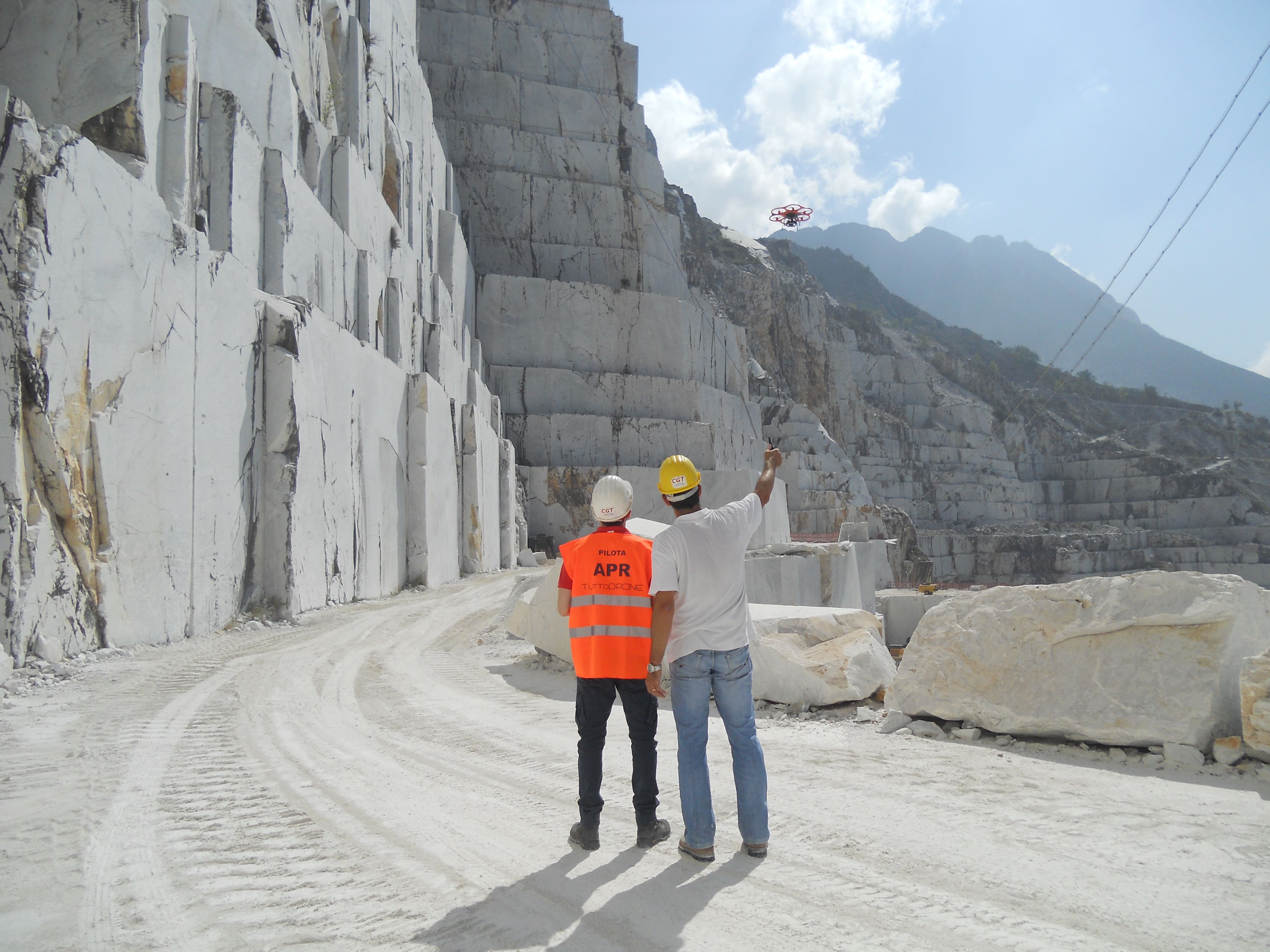 Two people and a small drone at a marble quarry during rock-slope imaging