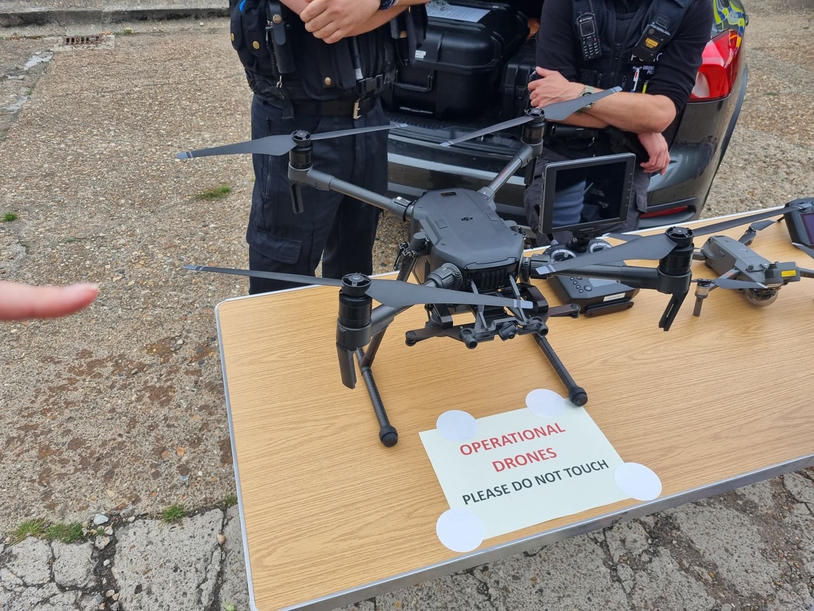 Large camera-equipped multirotor and smaller drone displayed with controllers beside uniformed personnel