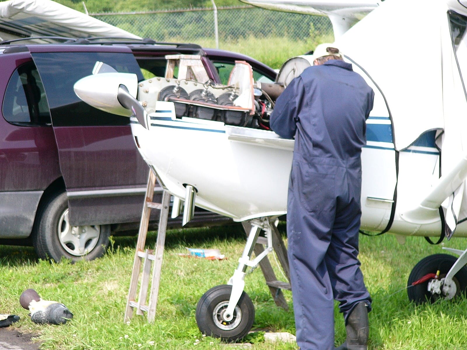 A mechanic working at the exposed engine of a Cessna 172 beside a service vehicle
