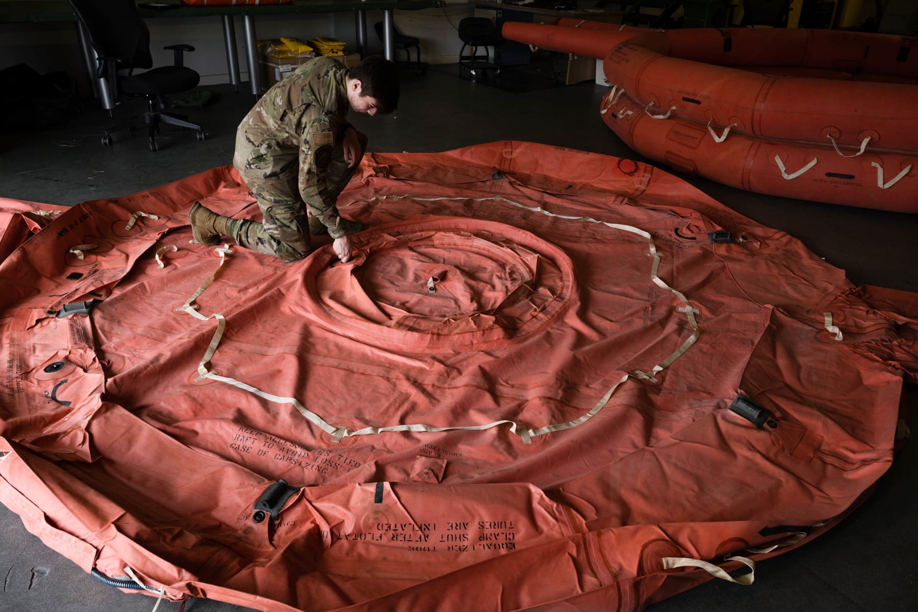 Air Force technician inspecting an unfolded orange emergency life raft in2022