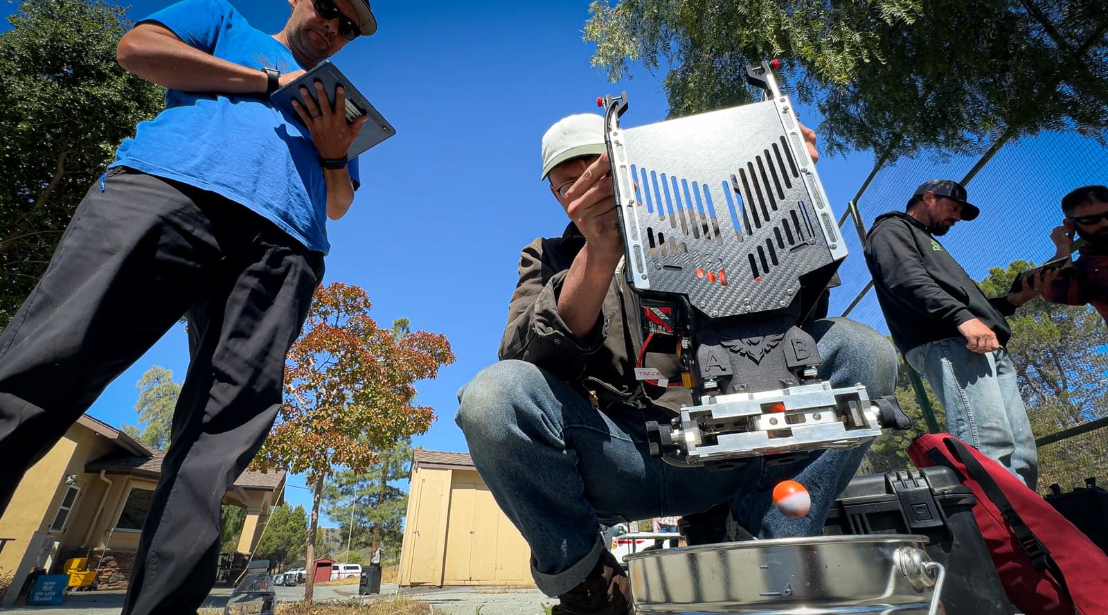 Personnel examining aerial ignition equipment outdoors while another person records information on a tablet