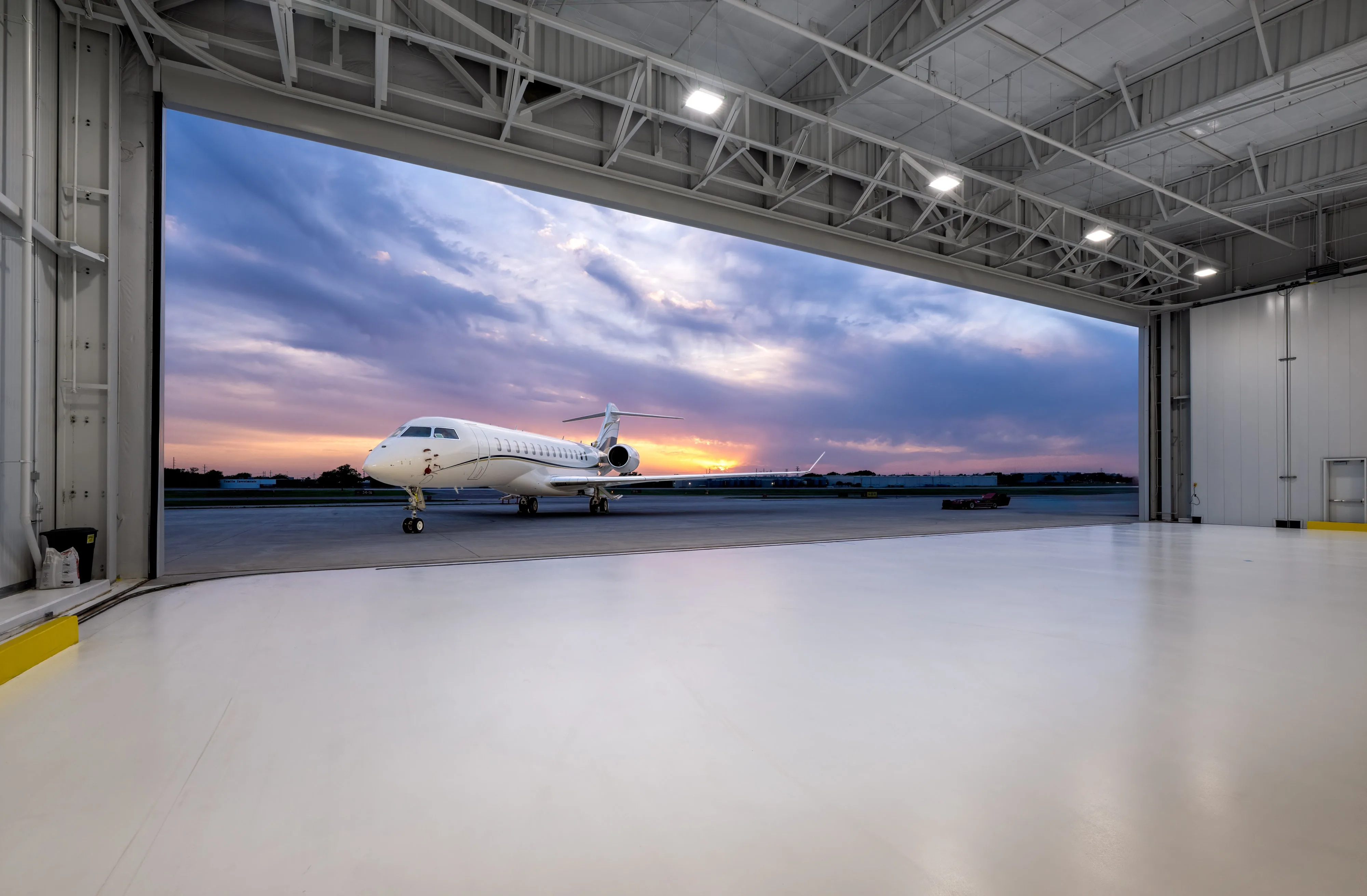 Business jet viewed from inside a large aircraft hangar at sunset